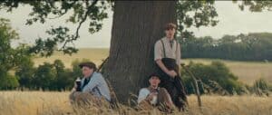 Young men resting under a large oak tree in a countryside field, promoting community and growth.