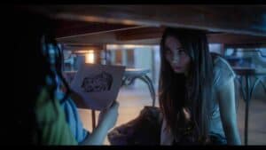 Suspicious woman hiding under table warns of danger in a thriller scene.